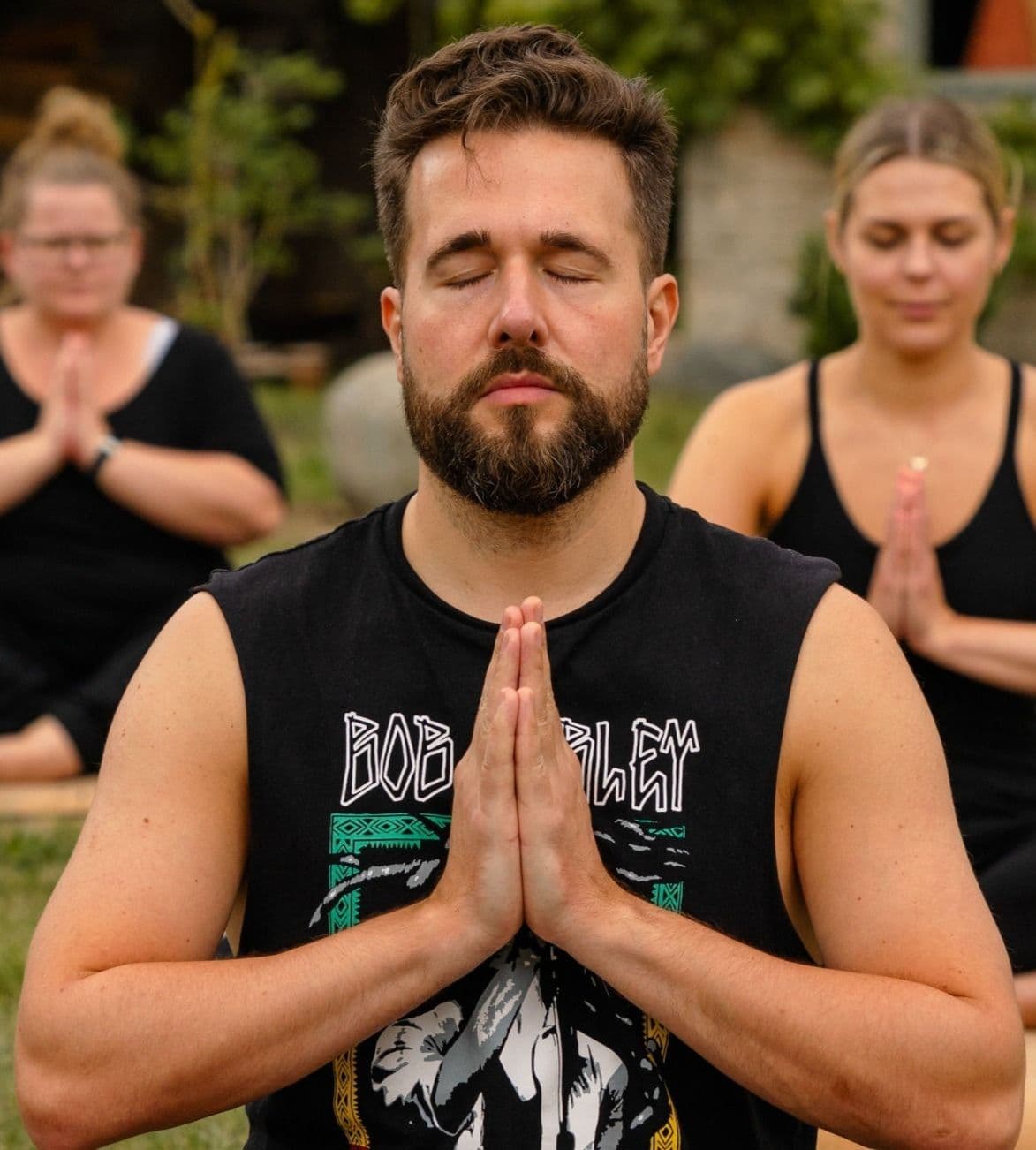 Meditation in der Gruppe im Freien, Hände in Gebetshaltung am Herzchakra, Gesichter entspannt
