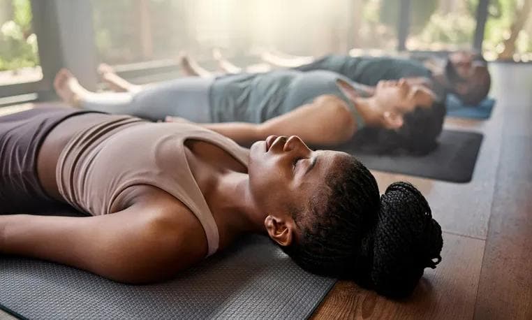 Übende ruhen mit geschlossenen Augen in Savasana auf ihren Yogamatten, tiefe Entspannung