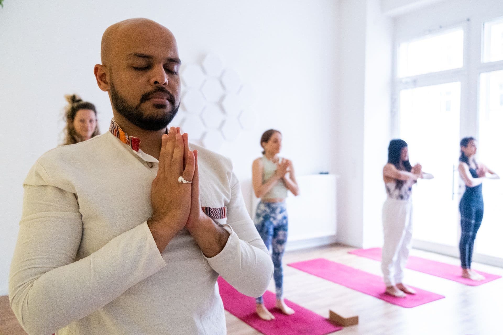 Ein Teilnehmer meditiert mit Händen am Herzen in einem hellen Morgenkurs im Yogicescape Prenzlauer Berg Yoga Studio, Berlin